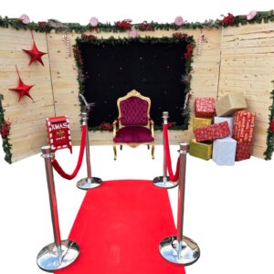 Un décor de Noël enchanteur composé d’un fond en bois, d’un pendrillon lumineux, d’un trône, d’un tapis de cérémonie 3×1 m, de six potelets, de faux cadeaux, d’une boîte aux lettres, d’une décoration soignée pour plonger votre événement dans la magie des fêtes. | Le Paradis De Tigrou